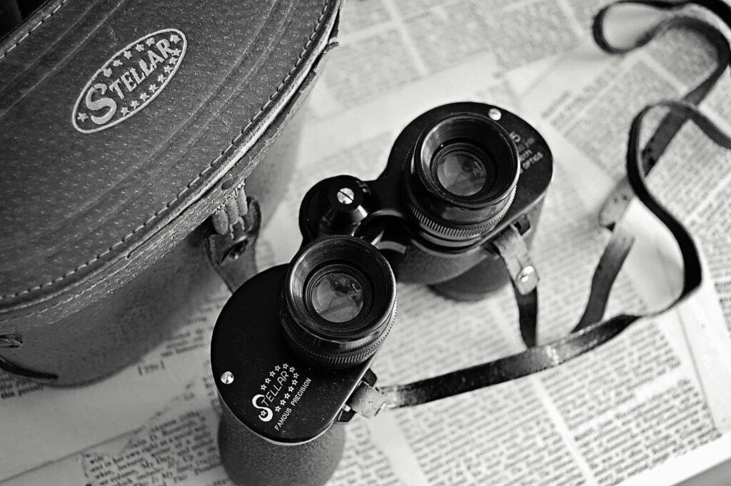 Classic vintage binoculars with a leather case laid on open newspapers, evoking nostalgia.